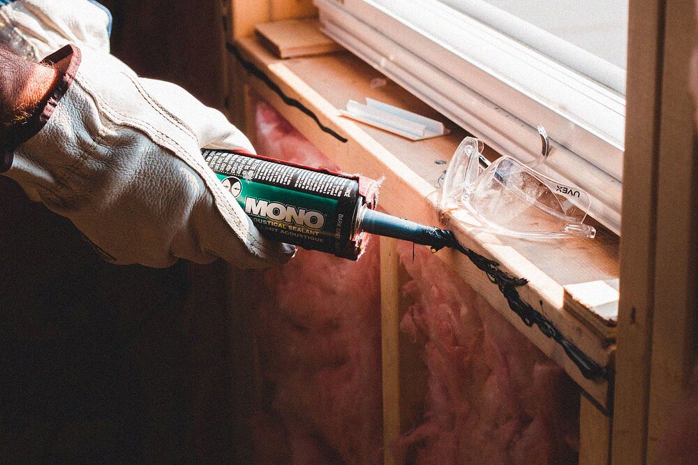 Gloved hand applying sealant along a seam on a building exterior
