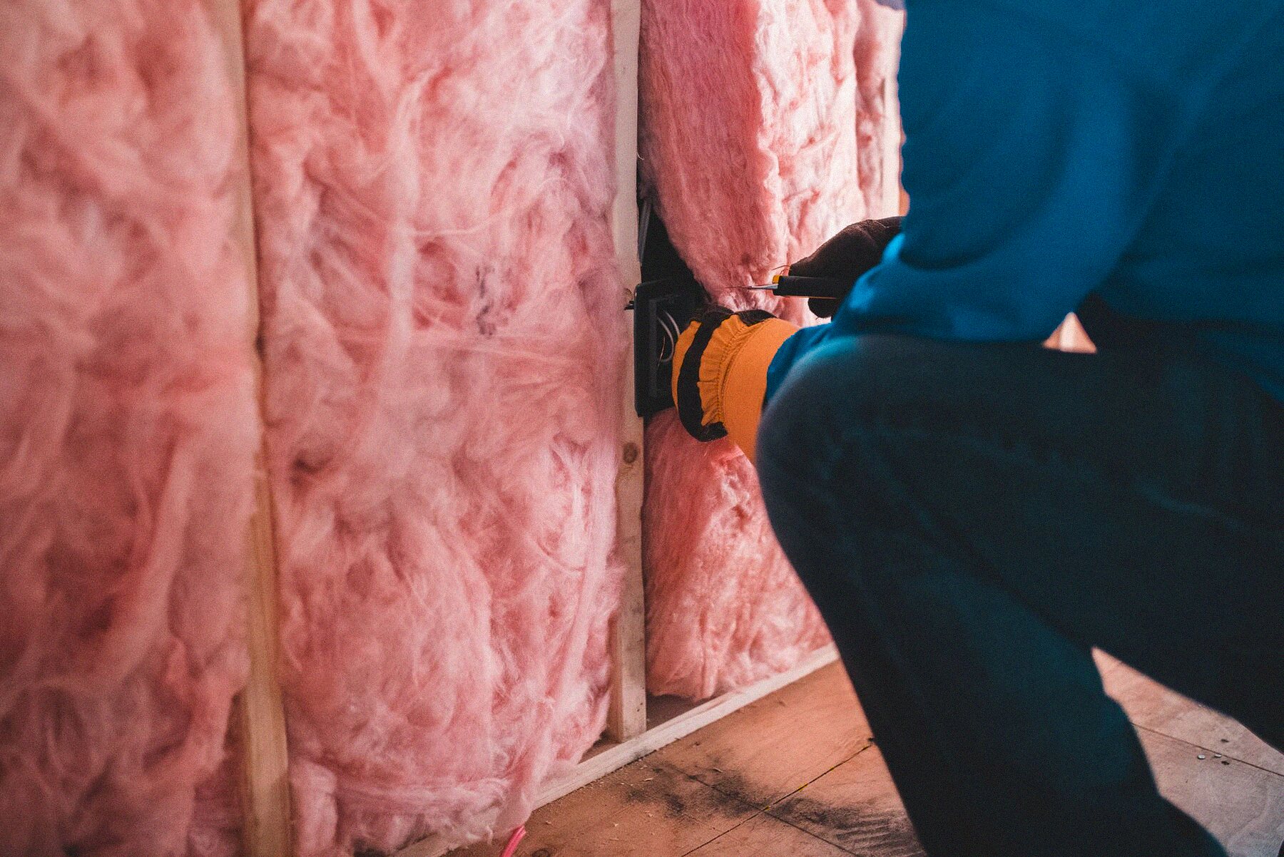 Technician in work gloves handling insulation inside a residential attic